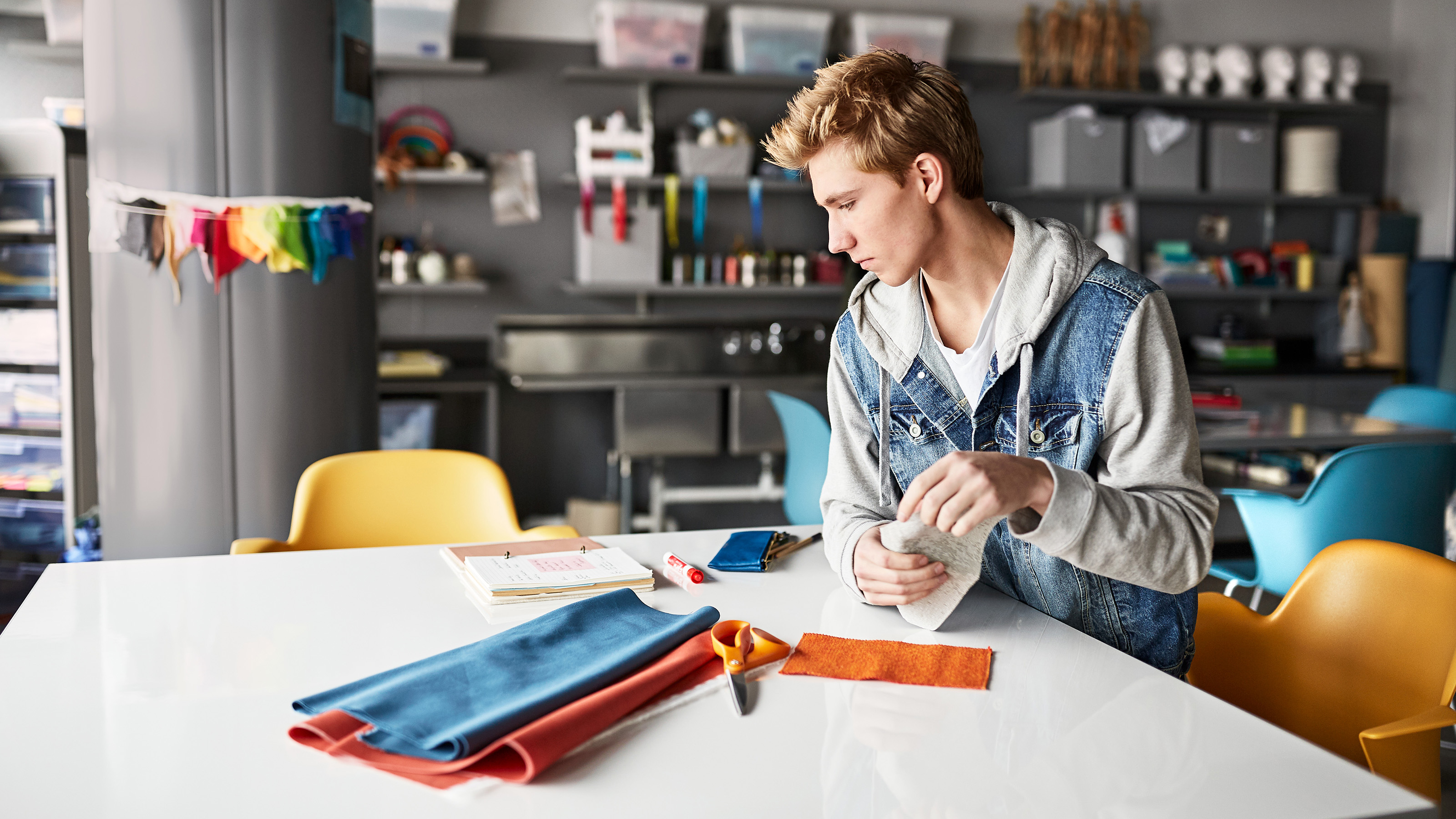 A young man sitting in a yellow Steelcase Node chair in front on a white table with different surface materials on top.