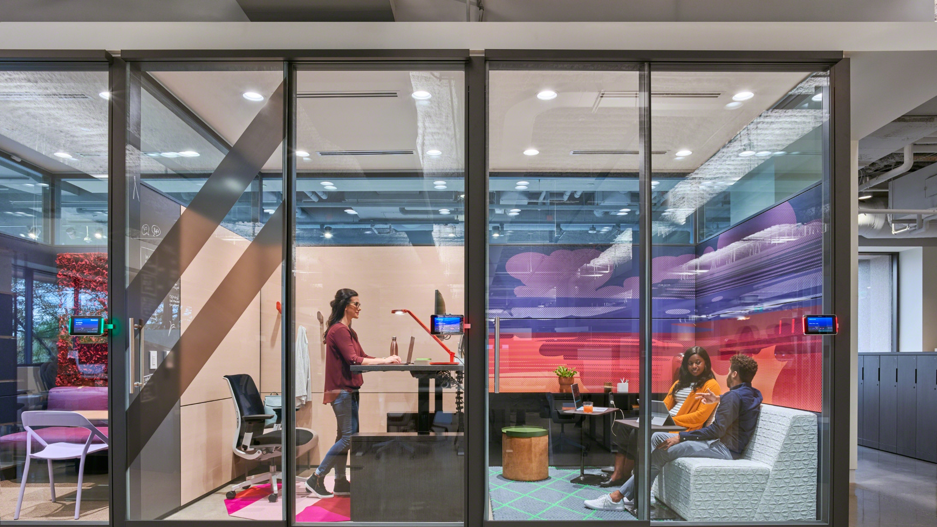Enclaves alongside each other with transparent doors and people working on a board and talking inside of them.